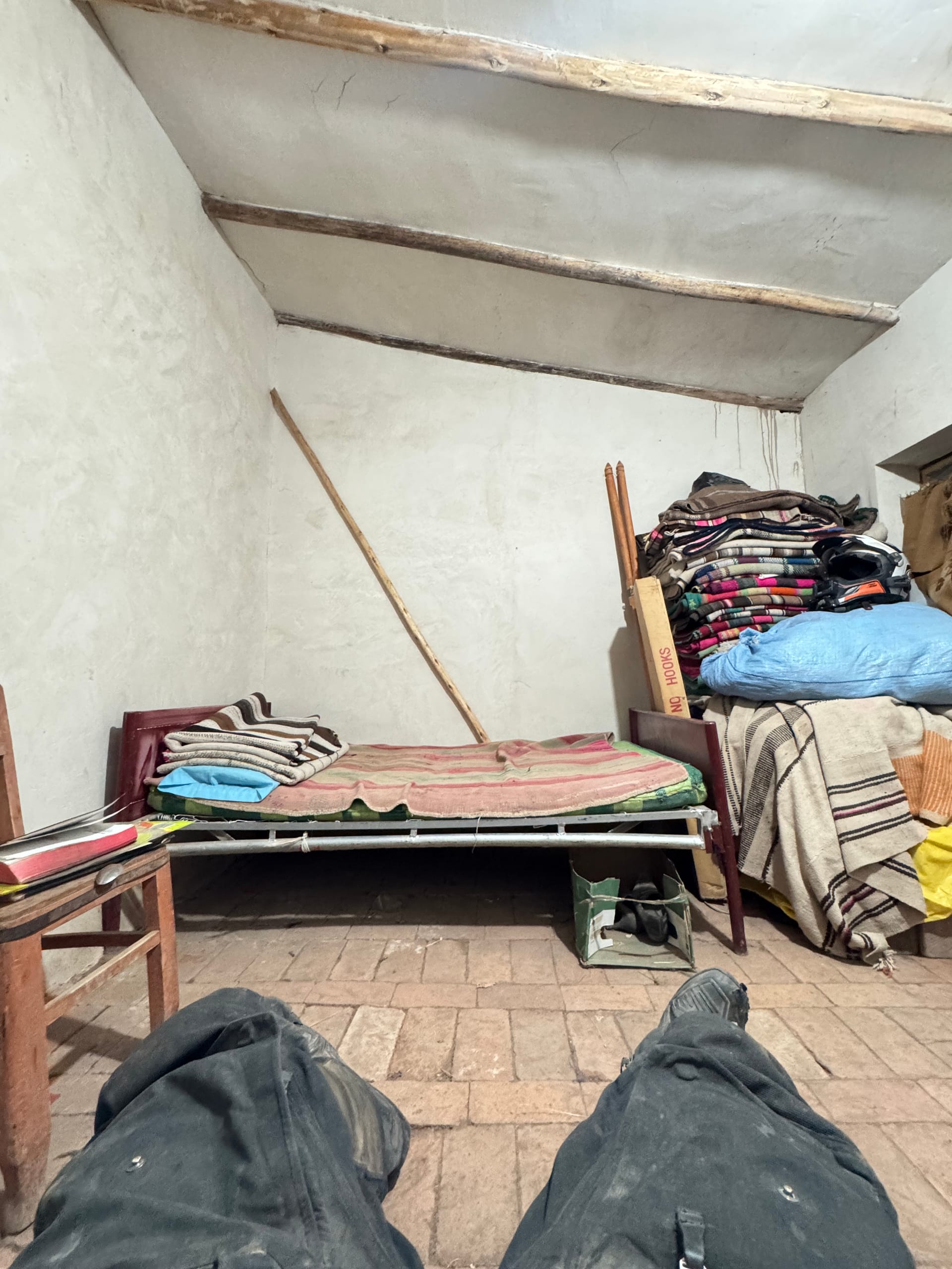 Chambre sommaire à Macha : lit en fer, couvertures empilées et casque de moto