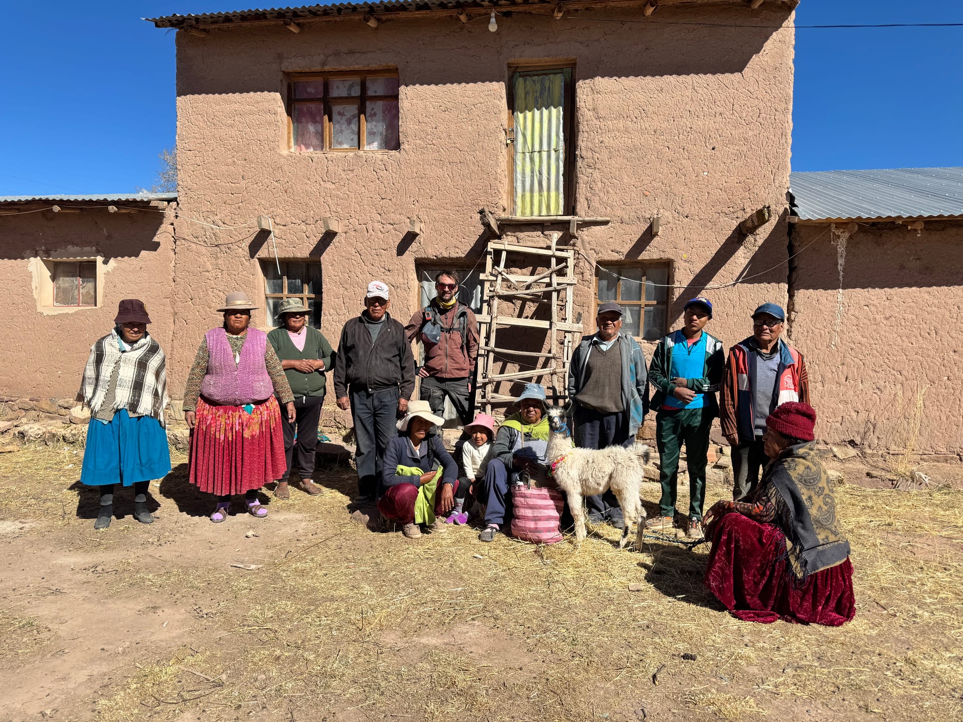 Habitants de Santiago de Andamarca posant devant une maison en adobe avec un bébé lama